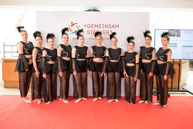 Tanzgruppe in schwarzen Kostümen auf rotem Teppich