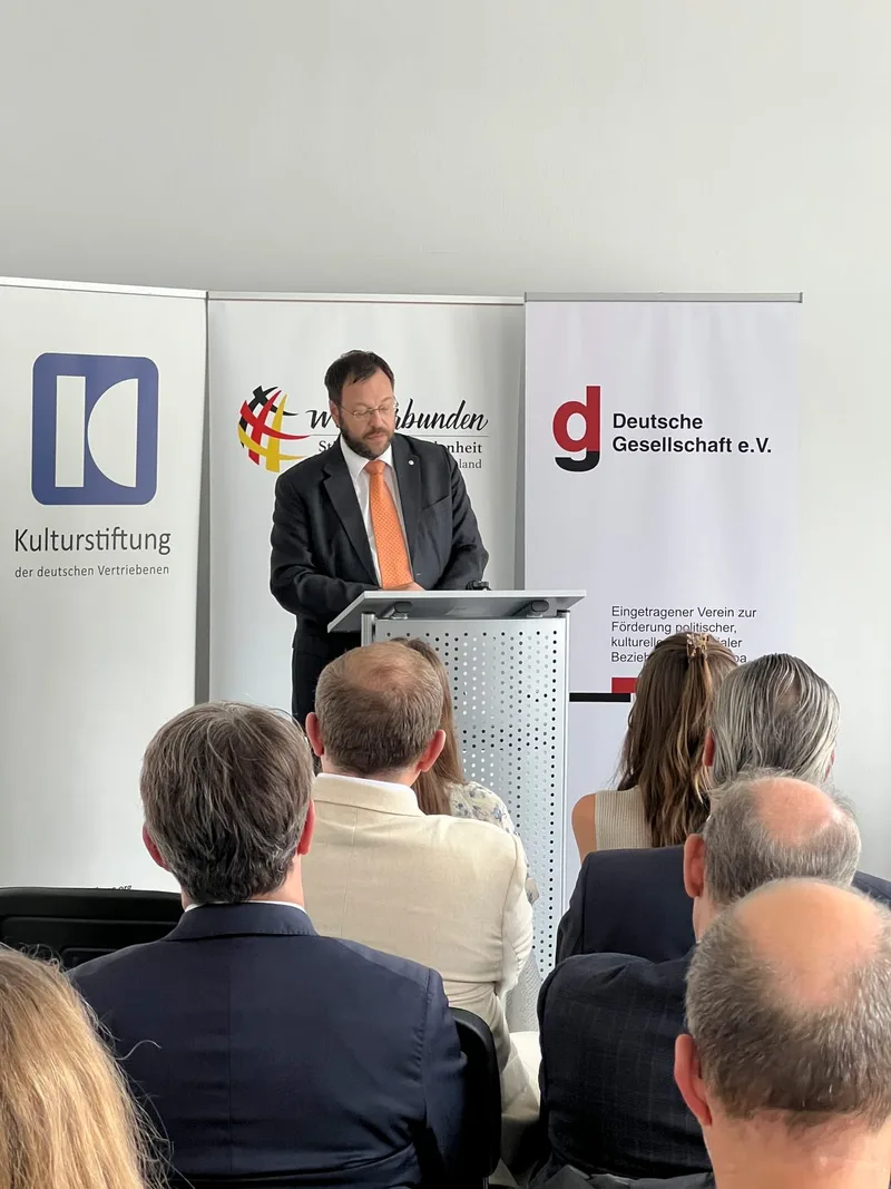 Ein Redner am Pult spricht vor Publikum und Bannern